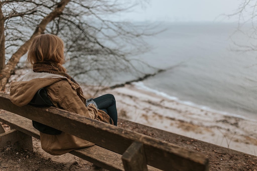 a woman sits on a bench overlooking a gloomy coastline