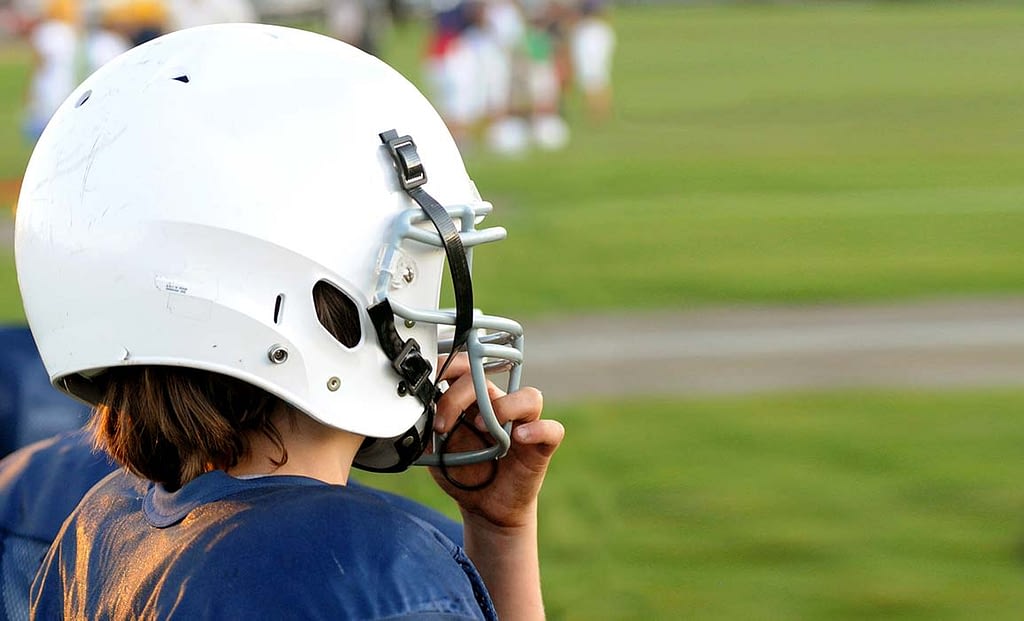 a child wearing a football helmet stands on the sidelines