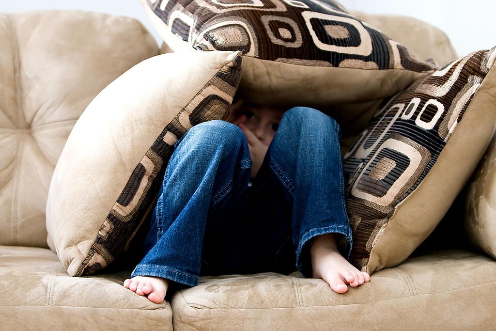 a young child hides under pillows while sitting on a couch