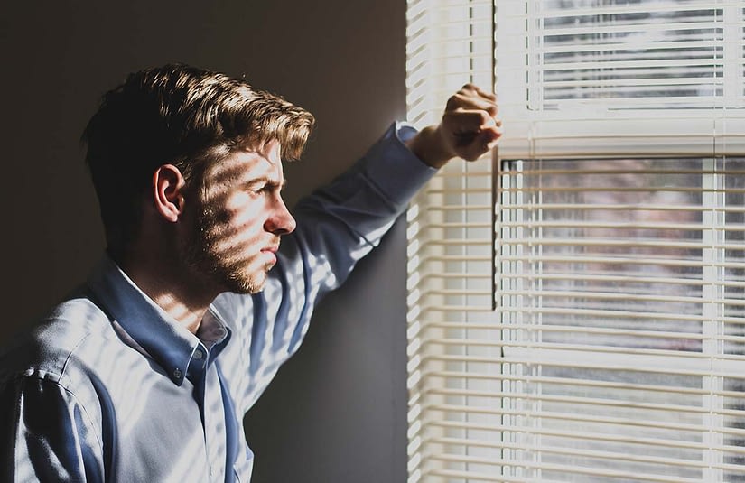a young man looks out a window, he looks sad